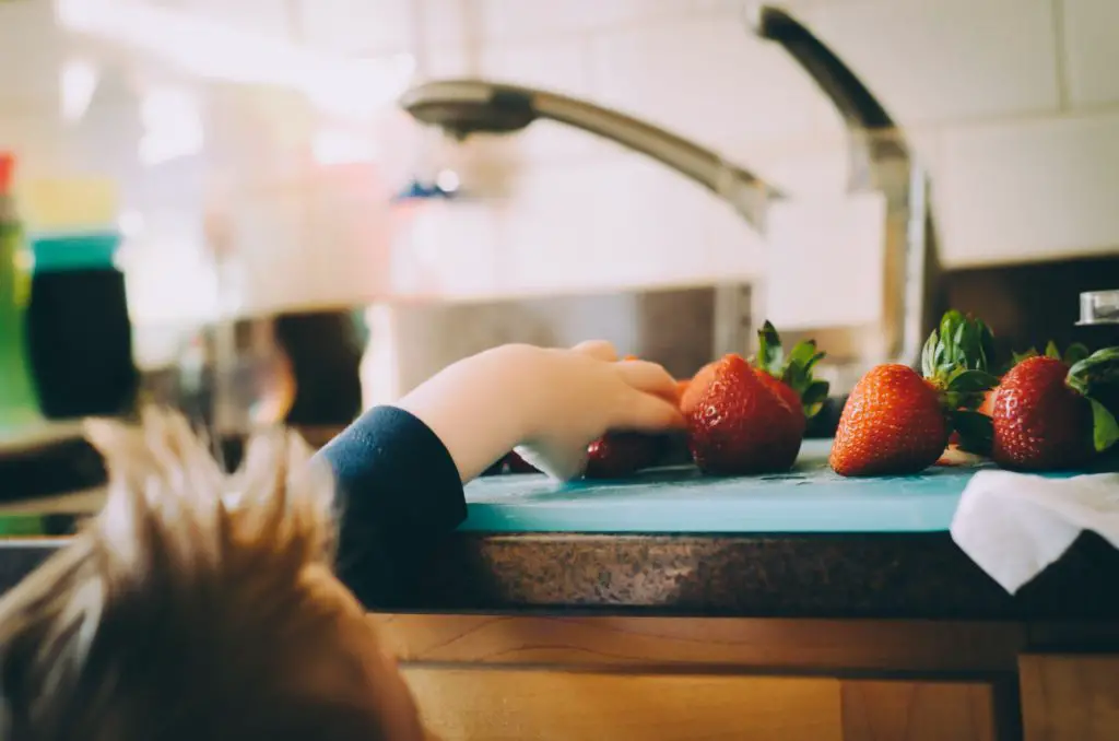 kid raising hand onto counter to grab healthy snack strawberries
